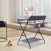 Child sitting on a portable changing table with a toy bag in a room.