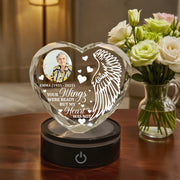 Heart-shaped glass memorial with engraved text and photo, placed on a wooden surface with flowers in the background.