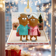 Decorative ornament with cartoon characters in bathrobes and text 'Annoying each other for 50 years and still going strong' against a festive background.
