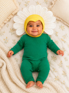 Baby in a green onesie with a white flower hat on a floral blanket